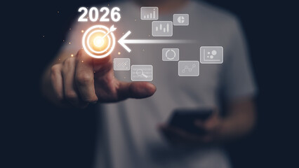 Human hand touch glowing digital target interface labeled 2026 with analytics icons, symbolizing strategic planning, business goal, data driven decision, future growth, innovation, technology roadmap.