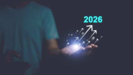 Human hand presenting glowing upward arrows and 2026, symbolizing future growth, business success, innovation, financial progress, strategic vision with digital technology concept and copy space.