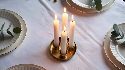 Close up of four white pillar candles burning brightly in a round brass candelabra on white tablecloth