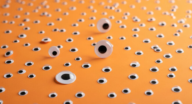 Many googly eyes scattered on orange background, creating playful, whimsical scene, perfect for craft, Halloween, or quirky design projects