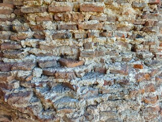 Ancient weathered red brick wall with crumbling mortar texture, showcasing historic architecture and aged masonry detail.