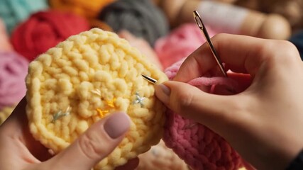 Close-up of hands sewing together colorful crochet pieces with a needle and yarn.
