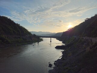 Beautiful sunset over a calm river valley with a distant bridge silhouetted between dark mountain ridges.