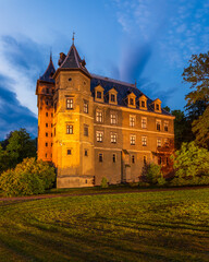 Illuminated historic castle at dusk surrounded by park greenery in Goluchow, Poland.