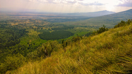 Wide panoramic view of a lush green valley surrounded by rolling hills and distant mountains under a bright blue sky with scattered clouds at Kijabe Hills in Kenya 
