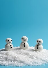 Three tiny handmade knitted snow figures standing upright on a mound of fluffy white winter material against a bright azure backdrop ,arrangement ,wintery ,winter