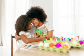 African American mother and daughter celebrate Easter and paint eggs with farbe and brush at home, woman with child decorate Easter eggs