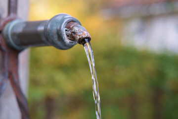 Clean water flowing from the old drinking fountain, blurred nature background. selective focus