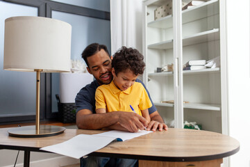 African American man and his son learn to write and draw at home at the table, teenager does homework with his father and smiles