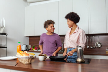 African-American woman and her son prepare chocolate butter and banana sandwiches in the kitchen, while teenager helps his mother prepare breakfast at home.