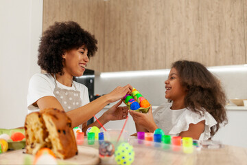 African American mother and daughter celebrate Easter and paint eggs with farbe and brush at home, woman with child decorate Easter eggs