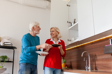 couple of elderly seniors are cleaning the kitchen and putting the dishes on the shelf, while grandma and grandpa are washing the dishes and doing housework together