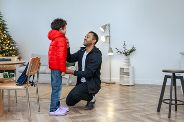 African American man helps his son put on his down jacket in the winter, father takes care of the child and gets him ready for school