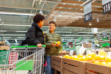 African American woman and her son shop for groceries at supermarket, and teenager and his mother choose fruits and vegetables at store