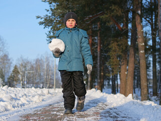 Young Boy Walk on camera Holding a Large Snowball on a Winter Path