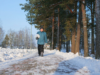 Young Boy Carrying a Large Snowball on a Snowy Path - Winter Walk: A Child in a Blue Jacket and Black Beanie Holding a Snowball in a Park