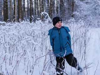 Young Boy Standing Beside Snow-Covered Brambles in a Winter Forest - Wintry Trail Walk: A Child in a Blue Jacket Enjoying a Snow-Drenched Woodland Path