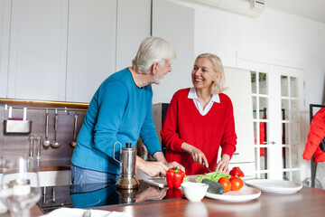 elderly couple of seniors are preparing food in the kitchen at home, grandparents are cutting vegetables and greens for salad together and talking