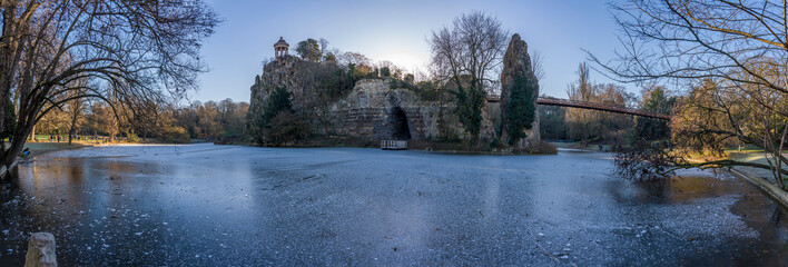 Paris, France - 01 04 2026: Buttes-Chaumont Park. Panoramic view of the frozen lake, belvedere island, Temple of the Sibyl, and vegetation in front