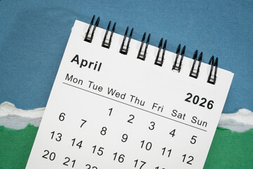 April 2026 - small spiral desktop calendar against art paper abstract, time and business concept