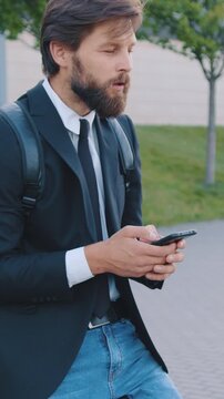Attractive man in jacket and jeanse sitting on his bicycle and using mobile to answer the sms on the big city building background at daytime,slow motion