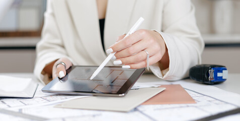 Female adult reviewing architectural plans on tablet in office, interior designer workplace