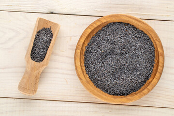 Dry poppy seeds with kitchen utensils on a wooden table, close-up, top view.