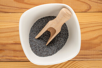 Dry poppy seeds with kitchen utensils on a wooden table, close-up, top view.