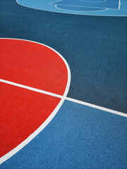 Red and blue outdoor basketball court surface. Rubberized textured sports flooring with white line markings and minimalist, geometric arrangement.