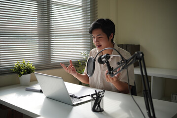Focused Asian man podcasting indoors, explaining ideas with hand gestures in a home office