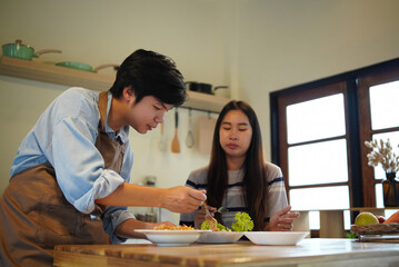 A young couple prepares and serves a homemade meal together in a warm, modern kitchen