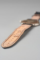 used brown leather wristwatch strap isolated neutral gray background, cracked and peeling inner surface damaged leather material, close-up and soft focus with copy space