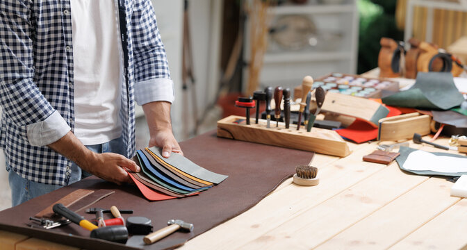 Male adult crafting leather in workshop with tools and fabric samples - Powered by Adobe