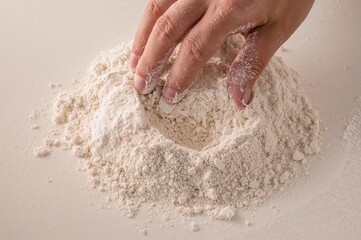 Baker hand shaping flour mound creating mixing well in soft light