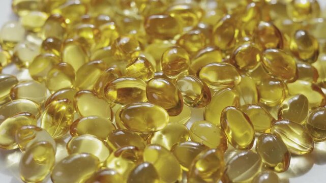 Top-down, close-up video of golden softgel capsules, like vitamin or fish oil supplements, slowly rotating on a turntable on white background showing concepts of healthcare, medicine, and nutrition.