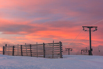 Ski lift at sunrise in Sweden with snow and colorful sky over mountains and hills