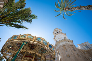 Tower of Cadiz Cathedral near Nostalgic Carousel and Palm Trees. Low Angle view 