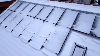Aerial view of solar panels on the roof of a house covered with snow on a frozen winter day.