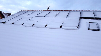 Aerial view of solar panels on the roof of a house covered with snow on a frozen winter day.