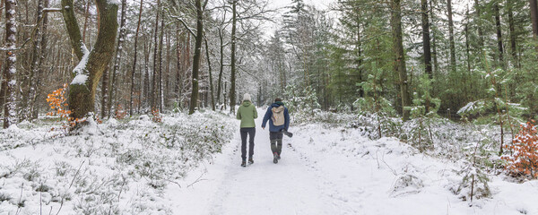 Two people walk along a snowy forest path, enjoying a quiet winter moment