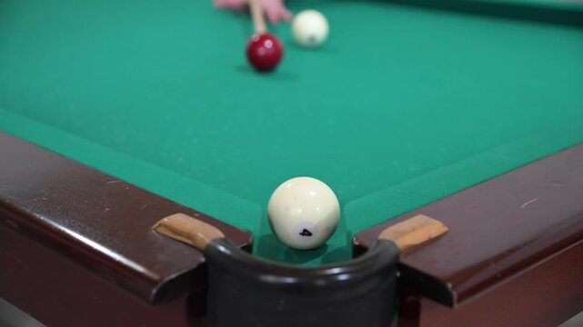 Hitting the ball with a cue and hitting the hole on the green background of the billiard table