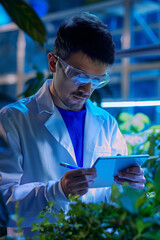 Scientist writing notes while inspecting plants in lab. Biotechnology concept.