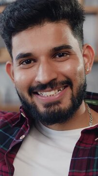 Close-up. Portrait petty man relax on comfort sofa smile staring at camera looks happy. Happy indian male sitting on sofa at home and looking at camera.