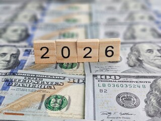 Banknotes and wooden blocks showing the year 2026 on a table with more money in the background...