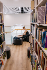 woman in library is reading book sitting on wide chair. young Caucasian woman in black dress flips through pages. education, scientific work. student in library.