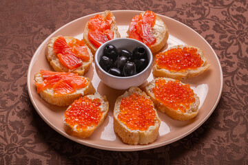 Canap s with red caviar and trout on a plate with olives on a brown tablecloth