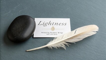 A single white feather and dark stone resting near a card about lightness, symbolizing release and ease