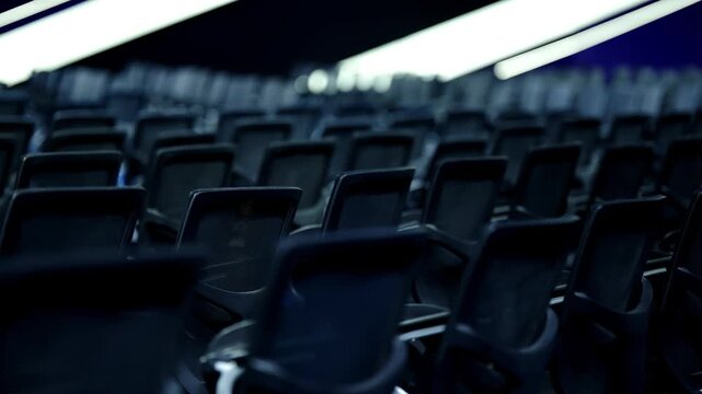 Empty ergonomic conference chairs fill a dimly lit auditorium, viewed from a low angle beneath linear ceiling lights, emphasizing repetition, depth, and contemporary design