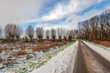 Agricultural landscape in winter. It has just snowed, and car tracks are visible on the country road. The photo was taken on a partly cloudy day in January.