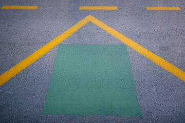 Road markings and urban infrastructure. Closeup view of a gray asphalt road with yellow lines and green rectangular marking in the center